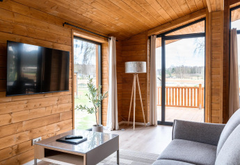 Moderne woonkamer in Lakehouse Scandi te Wilsumer Berge, Duitsland, met houten muren, tv en buitenzicht.
