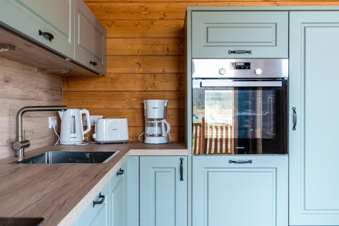 Moderne keuken met lichtgroene kasten, houten wanden en toestellen in Lakehouse Scandi, Wilsumer Berge, Duitsland.