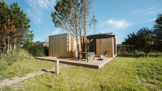 Casa pequeña de madera en De Klepperstee, Países Bajos, con terraza exterior, muebles y sombrilla de jardín.
