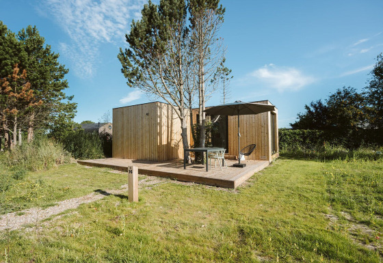 Klein houten huisje bij vakantiepark De Klepperstee in Nederland, met terras, parasol en buitenzitje.