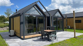 Tiny house moderna Cosy house presso Camping Si-Es-An, Olanda, con patio e ampie vetrate luminose.