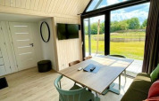 Interior luminoso y acogedor de tiny house con grandes ventanales y vista al exterior en Camping Si-Es-An, Países Bajos.