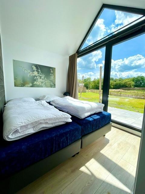 Dormitorio luminoso con grandes ventanales en una tiny house en Camping Si-Es-An, Países Bajos, vista a la naturaleza.