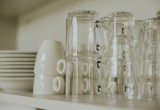 Tazas de cristal apiladas y platos en un estante en la tiny house Cosy house de Camping Si-Es-An, Países Bajos.