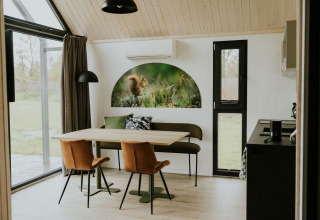 Interior de una tiny house en Camping Si-Es-An, con mesa de comedor, ventanales y arte de ardilla.