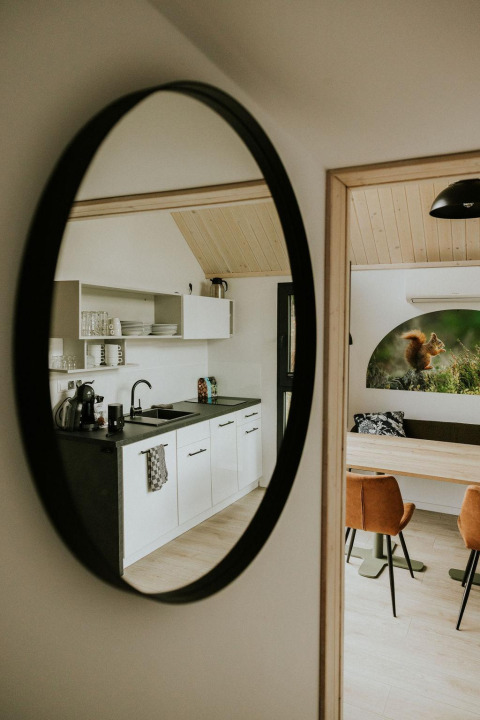 Moderne kitchenette en eethoek van een tiny house gereflecteerd in een spiegel bij Camping Si-Es-An, Nederland.