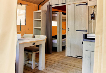 Interior of a safari tent with wood furniture, bunk beds, and shelving at Campeggio Gasparina, Italy.