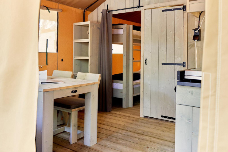 Interior of a safari tent with wood furniture, bunk beds, and shelving at Campeggio Gasparina, Italy.