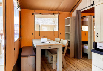 Interior view of a Villatent Outback safari tent with dining table, chairs, bench, shelves and bunk beds.