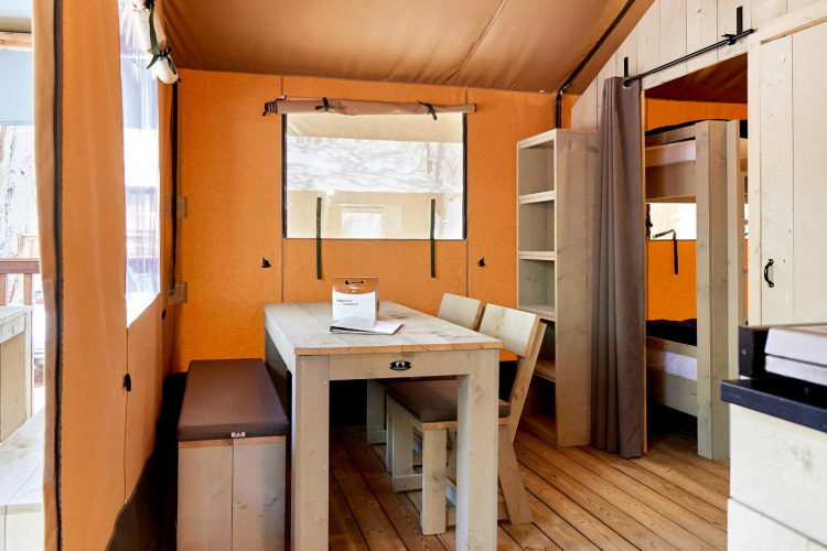 Interior view of a Villatent Outback safari tent with dining table, chairs, bench, shelves and bunk beds.