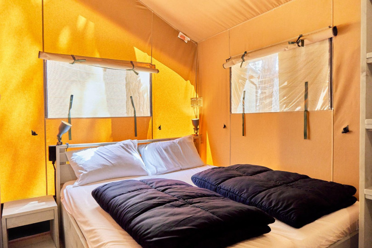 Interior of a safari tent at Villatent Outback with a double bed, pillows, dark duvets, and windows.