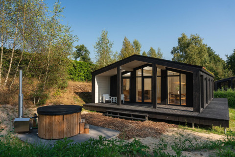 Casa pequeña negra con grandes ventanales y bañera de hidromasaje de madera en Wilsumer Berge, Alemania.