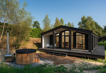 Zwart tiny house met grote ramen en een houten buitenjacuzzi bij Wilsumer Berge in Duitsland.
