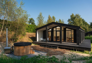 Tiny house nera con grandi finestre e vasca idromassaggio esterna in legno a Wilsumer Berge, Germania.