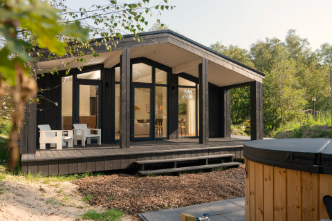 Tiny house Hills avec jacuzzi à Wilsumer Berge en Allemagne, façade noire, terrasse bois et environnement naturel.