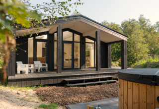 Tiny house Hills avec jacuzzi à Wilsumer Berge en Allemagne, façade noire, terrasse bois et environnement naturel.