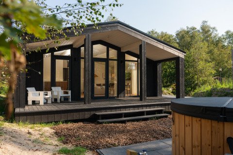 Tiny house ved Wilsumer Berge i Tyskland, med moderne sort facade, terrasse og udendørs varmtvandsbad.