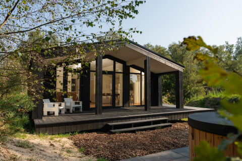 Lille sort træhus med store vinduer og veranda, omgivet af natur, Hills med spa ved Wilsumer Berge, Tyskland.