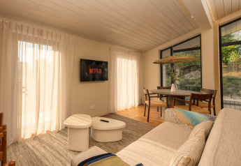 Woonkamer van een tiny house bij Wilsumer Berge, Duitsland, met bank, Netflix en eettafel in het zonlicht.