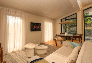 Woonkamer van een tiny house bij Wilsumer Berge, Duitsland, met bank, Netflix en eettafel in het zonlicht.