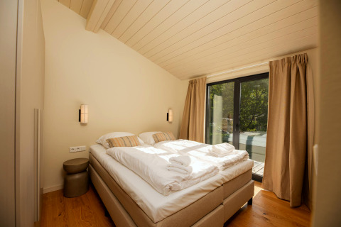 Chambre de la tiny house Hills avec lit double, grandes fenêtres et rideaux à Wilsumer Berge, Allemagne.