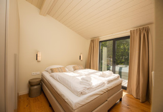 Dormitorio en la tiny house Hills con cama doble, grandes ventanales y cortinas en Wilsumer Berge, Alemania.