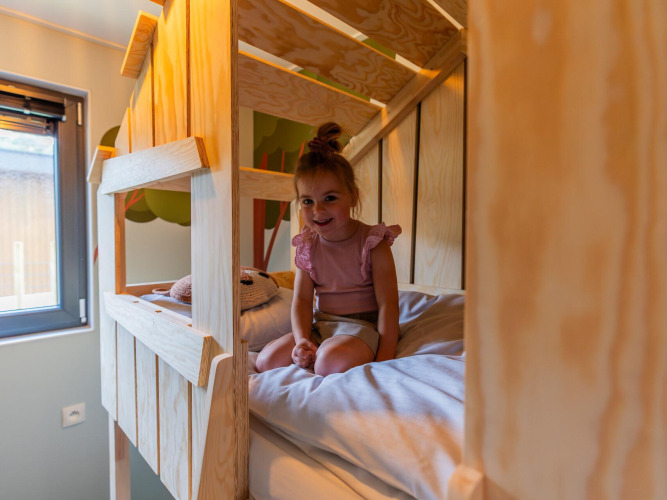 Smiling girl sitting on a bunk bed at Kids cottage lodge in Kaatsheuvel, Netherlands, wooden decor.
