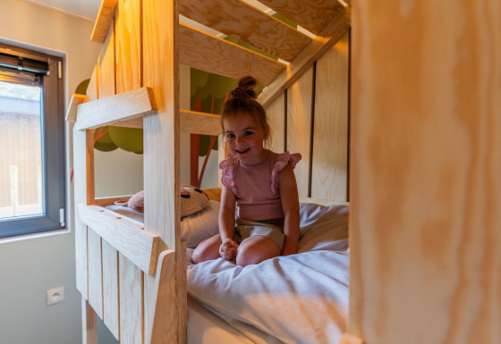 Niña sonriente sentada en una litera en el Kids cottage lodge de Kaatsheuvel, Países Bajos, decoración de madera.