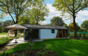 Casa Kids cottage en Kaatsheuvel, Países Bajos, rodeada de césped verde y árboles altos en un día soleado.