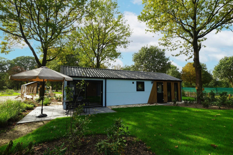Kids cottage lodge in Kaatsheuvel, Netherlands, surrounded by green lawn and tall trees on a sunny day.