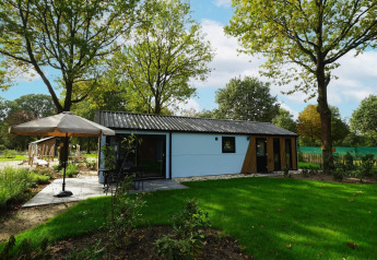 Billede af Kids cottage lodge i Kaatsheuvel, Holland, omgivet af grønne træer og en solrig have.