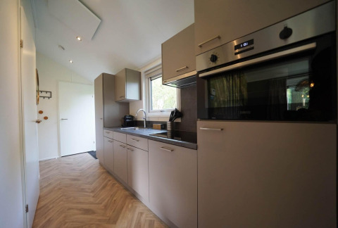 Cucina moderna al Kids cottage a Kaatsheuvel, Paesi Bassi, con mobili grigi, forno e pavimento in legno.