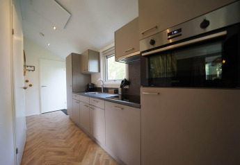 Cucina moderna al Kids cottage a Kaatsheuvel, Paesi Bassi, con mobili grigi, forno e pavimento in legno.