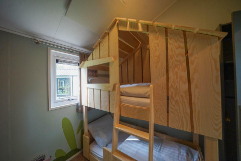 Stapbed met houten frame in Kids cottage in Kaatsheuvel, Nederland, naast een raam met zicht buiten.