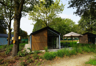 Vue du lodge Kids cottage à Kaatsheuvel, Pays-Bas, entouré de verdure, arbres et coin terrasse extérieure.