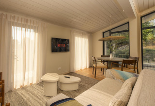 Sala luminosa en The Hills tiny house en Wilsumer Berge, Alemania, con sofá, mesa de comedor y TV con Netflix.