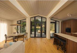 Interior luminoso y moderno de tiny house con acabados de madera, grandes ventanas y vistas a la naturaleza.