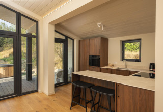 Modern kitchen inside The Hills tiny house with large windows and natural wood cabinets at Wilsumer Berge, Germany.