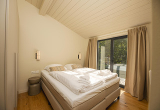 Dormitorio luminoso en la tiny house The Hills con cama doble, grandes ventanales y vistas, Wilsumer Berge, Alemania.