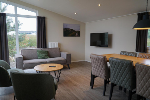 Woonkamer van Dune Lodge bij EuroParcs Parc du Soleil met bank, eettafel en uitzicht door groot raam.