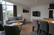 Stue i Dune Lodge ved EuroParcs Parc du Soleil med sofa, spisebord og vindue med udsigt til naturen.
