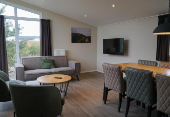 Woonkamer van Dune Lodge bij EuroParcs Parc du Soleil met bank, eettafel en uitzicht door groot raam.