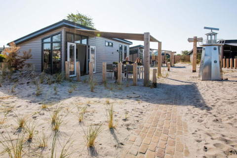 Moderne Dune Lodge ved EuroParcs Parc du Soleil i Holland, omgivet af sand og græs, solrig dag.