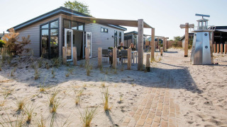Dune Lodge moderne à EuroParcs Parc du Soleil aux Pays-Bas, entourée de sable et d’herbes de dunes.