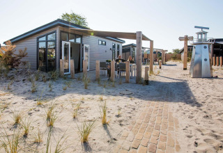 Moderne Dune Lodge ved EuroParcs Parc du Soleil i Holland, omgivet af sand og græs, solrig dag.