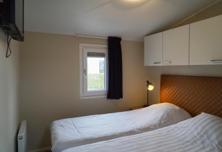 Dormitorio con dos camas individuales, ropa de cama blanca, ventana, armarios y lámpara en Dune Lodge.
