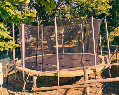 Trampolín con red de seguridad rodeado de árboles en Camping Lucherino, parque vacacional en la Toscana.