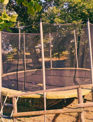 Trampolín con red de seguridad rodeado de árboles en Camping Lucherino, parque vacacional en la Toscana.