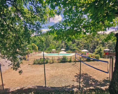 Vue sur une piscine et un terrain de volley entourés de verdure au Camping Lucherino en Toscane, Italie.
