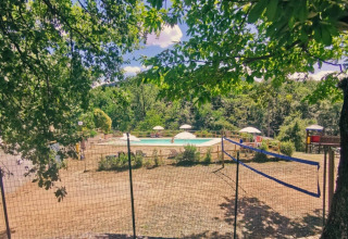 Vue sur une piscine et un terrain de volley entourés de verdure au Camping Lucherino en Toscane, Italie.